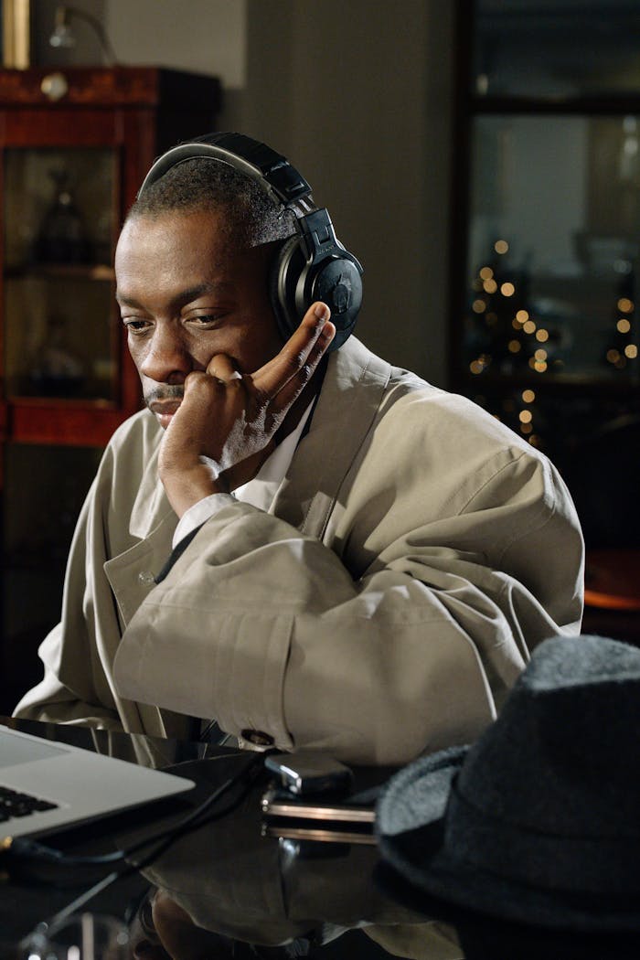 A mysterious detective in trench coat listens intently with headphones in a dimly lit room.